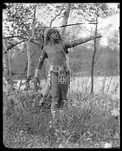 A man wearing Native American headdress and clothing posing outdoors