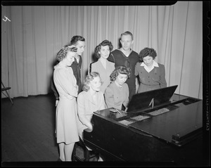 Servicemen singing with women at a piano