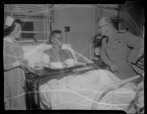 Military personnel speaking with an injured person in a hospital bed, likely military personnel injured in the U.S.S. Bennington aircraft carrier explosion off coast of Rhode Island