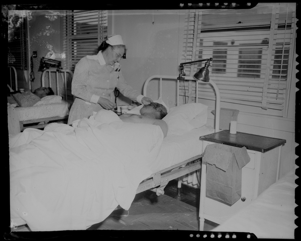 An injured person lying in a hospital bed being tended to by a nurse ...