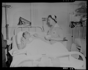 An injured person lying in a hospital bed being tended to by a nurse, likely military personnel injured in the U.S.S. Bennington aircraft carrier explosion off coast of Rhode Island