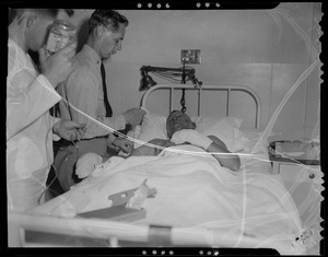 Military personnel speaking with an injured person in a hospital bed, likely military personnel injured in the U.S.S. Bennington aircraft carrier explosion off coast of Rhode Island
