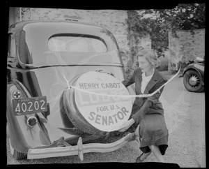 Woman holding a "Henry Cabot Lodge for U.S. Senator" sign over the rear spare tire of a car