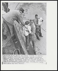 Small Victims of Flood--West Virginia National Guardsmen unload children rescued from flooded homes onto higher ground here today. Behind Guardsman, young boy rescued clings to leg of father, who holds baby of family.