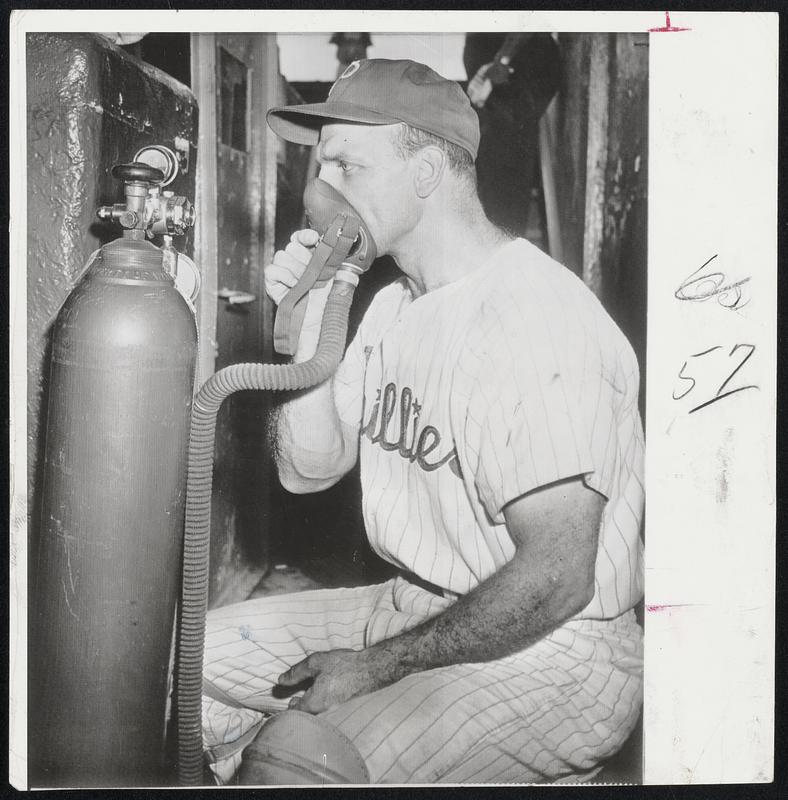 Andy Seminick of the Phillies takes a whiff of oxygen from tank that has been installed in dugout. Trainer Frank Wiechec feels the oxygen helps the players regain strength on hot days.
