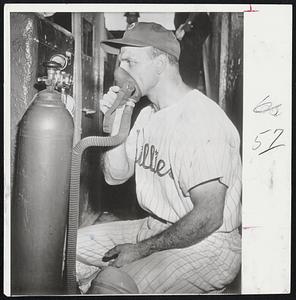 Andy Seminick of the Phillies takes a whiff of oxygen from tank that has been installed in dugout. Trainer Frank Wiechec feels the oxygen helps the players regain strength on hot days.