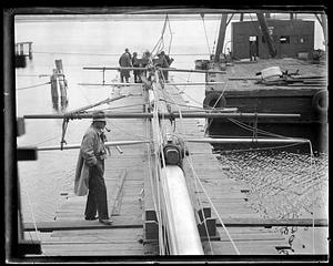 A man, possibly Gerard B. Lambert, looking at a large spar on a dock