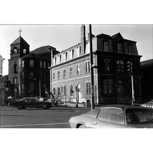 Street view of La Alianza Hispana's headquarters, 409 Dudley Street, Roxbury, Massachusetts, the three-story brick building at the intersection, with cars driving by