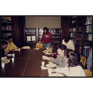 Staff members and two children, seated around tables, eat and converse