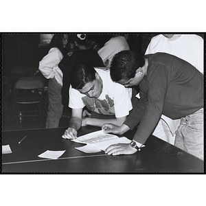 Two young men leaning over a table and looking at papers during the Boys and Girls Clubs of Boston 100th Anniversary Celebration event at the Charlestown Boys and Girls Clubhouse