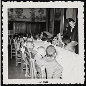 The Kiwanis Club's president Les Oshry stands at a table of seated boys at a birthday party