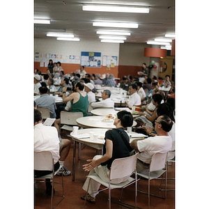 Photographer crouched among several tables of people at a Chinese Resident Association celebration