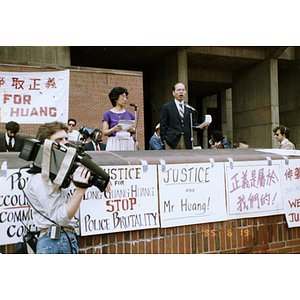 Asian man speaks at a rally for Long Guang Huang at City Hall Plaza in Boston, with Chinese Progressive Association director Suzanne Lee