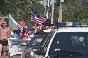 Police escort leading the approaching parade, with man dressed in Puritan costume ringing a bell : Provincetown Carnival parade