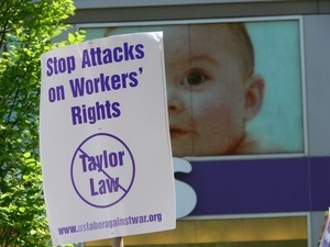 Antiwar marchers in the streets of New York with sign reading 'Stop attacks on workers' rights' (US Labor Against War) passing by a Toys R Us store with images of babies