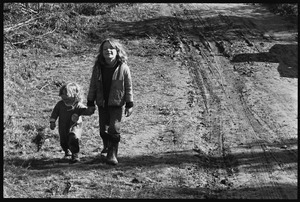 Young girl leading a toddler by hand down a muddy road, Earth People's Park