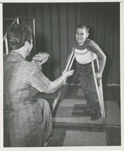 Boy walks with crutches toward physical therapist