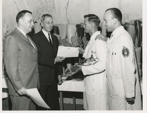 James Burrows presents a certificate of completion of training to a 1964 Prosthetics and Orthotics training graduate while two other men look on