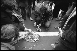 Anti-Vietnam War protesters kneeling on the ground, preparing to burn miniature American flags distributed by the Boy Scouts during the Counter-inaugural demonstrations, 1969