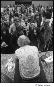 Ram Dass seated on stage at the College of Marin, talking to audience members