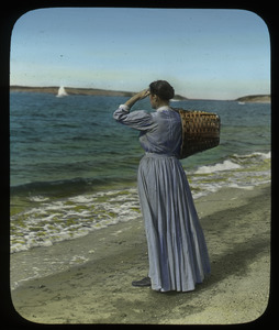 Woman with basket on beach looking over ocean inlet