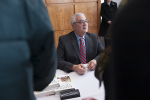 Congressman Barney Frank seated at a table in the Student Union Ballroom stage, UMass Amherst, signing copies of his biography