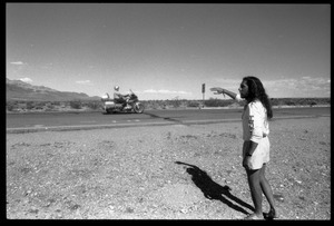 Peace encampment activist waving at a passing vehicle on the road near the entrance to the Nevada Test Site