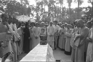 Van's family surrounding casket before lowering into grave. Van's youger son holds portrait while his widow looks on; Saigon.