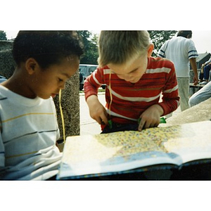 Two young boys look at a picture book, seated outside.