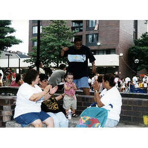 Three women and a toddler clapping their hands as they rest on a ledge at Festival Betances.