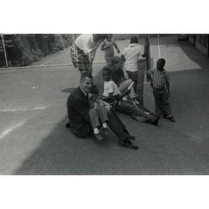 A seated man holds a boy in his lap as other boys look on during Tom Sawyer Boy