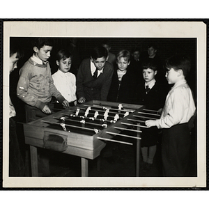 Two boys play foosball as other boys look on