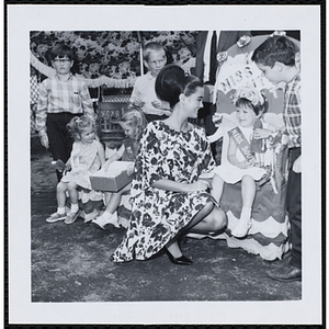 The Little Sister Contest winner sits on her throne with a doll while posing with her brother and a judge