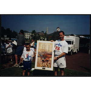 A boy and a man pose with framed print at the Battle of Bunker Hill Road Race
