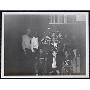 The Boys' Club of Boston basketball team, their coach, and team mangagers pose for a group shot with a trophy