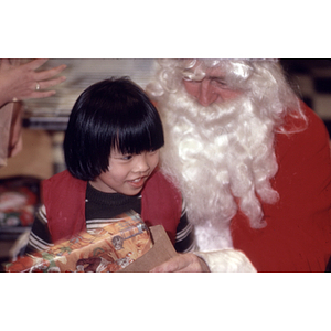 Young boy holds a present while sitting on Santa's lap at a Chinese Progressive Association Christmas party