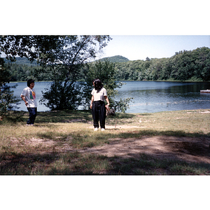 Two young women stand near the waterfront of a lake