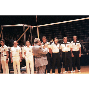 Man plays the trumpet into a microphone on a volleyball court