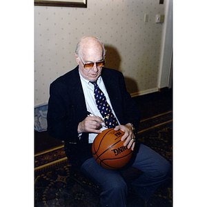 Arnold Jacob "Red" Auerbach, former Boston Celtics coach, autographs basketball