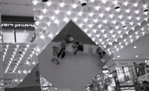 Commune member distributing Free Spirit Press in an indoor shopping mall: image of magazine distributors in reflection