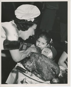 Woman in chef's hat feeding turkey to child in wheelchair