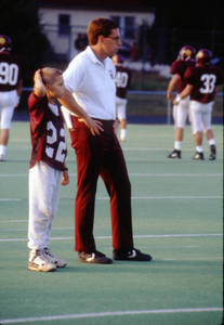 Head Coach Mike DeLong with a young boy on the sidelines at a football game, 1988