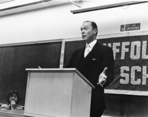 Roger Moore speaking in a Suffolk University classroom from behind podium