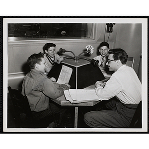 Three boys sit at a WHDH microphone console in the studio with a broadcaster