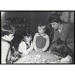Children play the Candyland board game as a woman looks on