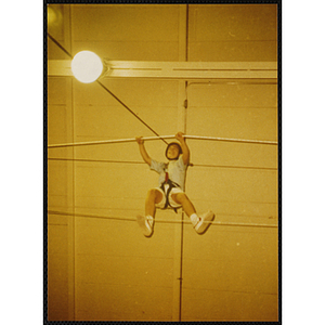 A boy walks across a gymnasium on a rope