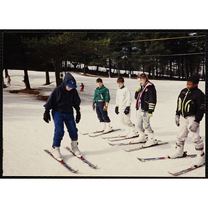 A group of children take ski instruction from a boy at a resort