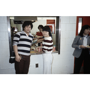 Two Chinese Progressive Association youth members stand at a kitchen serving window