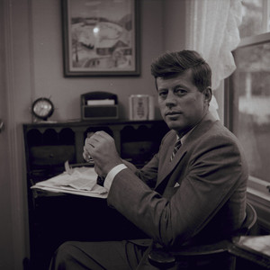 Portrait of John F. Kennedy, full face, seated at his desk, 1957