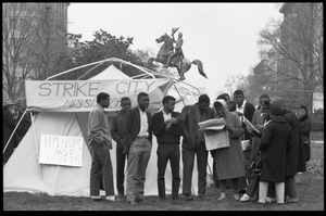 Strikers and supporters milling about outside a tent, a woman showing a newspaper to interested young men, statue of Lafayette in the background